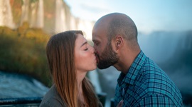 Ein Foto eines Paares, das einen Kuss mit Wasserfällen im Hintergrund teilt